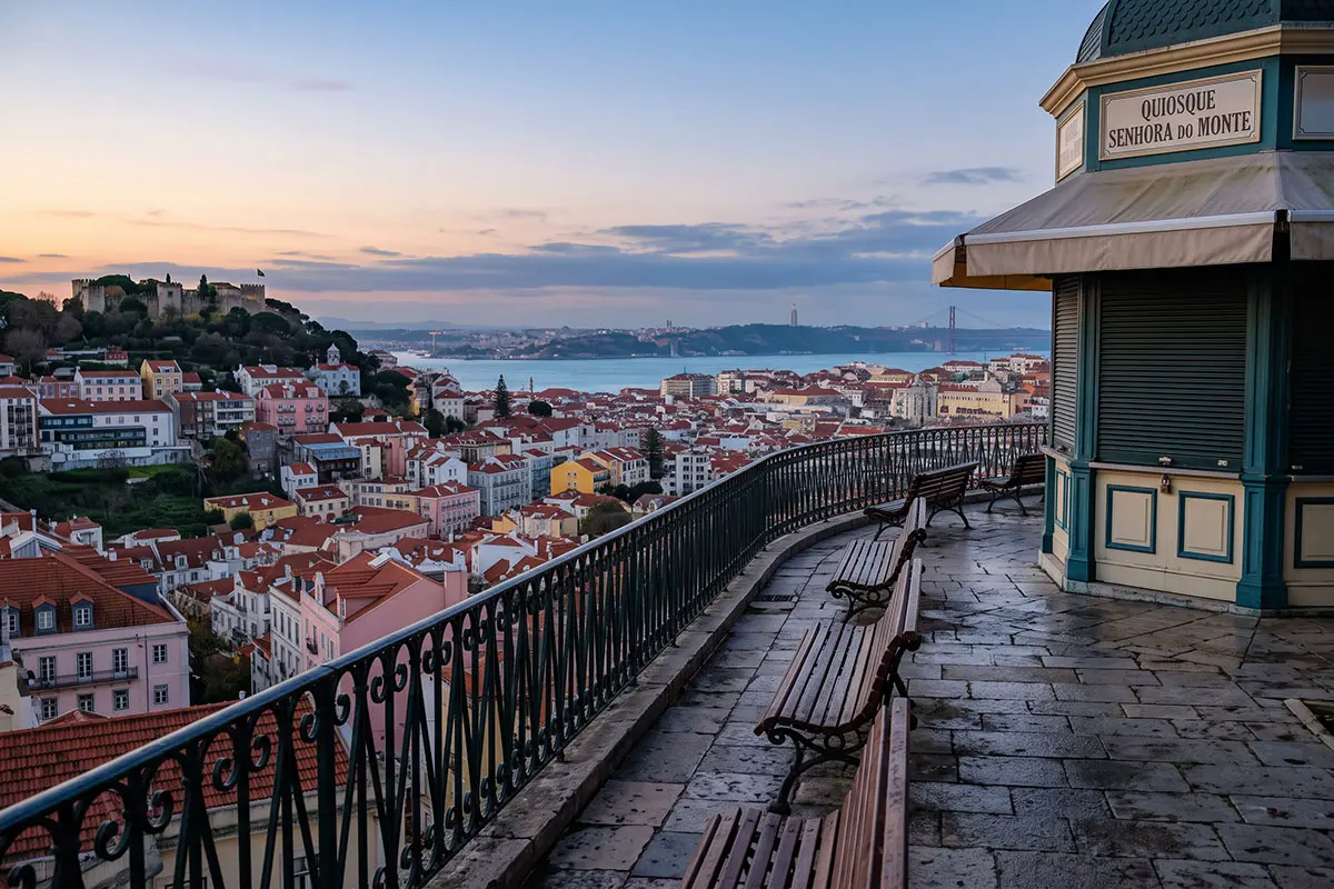 O miradouro da Senhora do Monte vazio ao amanhecer, sobre os telhados de Lisboa, o castelo e a Ponte 25 de Abril, sem multid&otilde;es