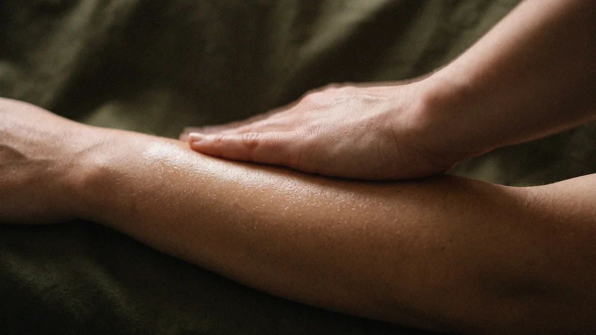 Close-up of a slow, gentle stroke along the forearm during a massage, skin glistening with oil